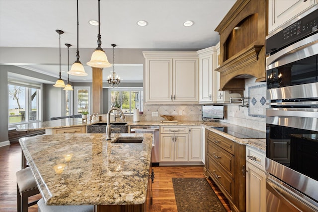 kitchen with decorative light fixtures, backsplash, appliances with stainless steel finishes, a center island with sink, and dark wood-type flooring