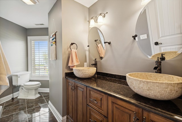 bathroom with tile floors, vanity with extensive cabinet space, toilet, and dual sinks