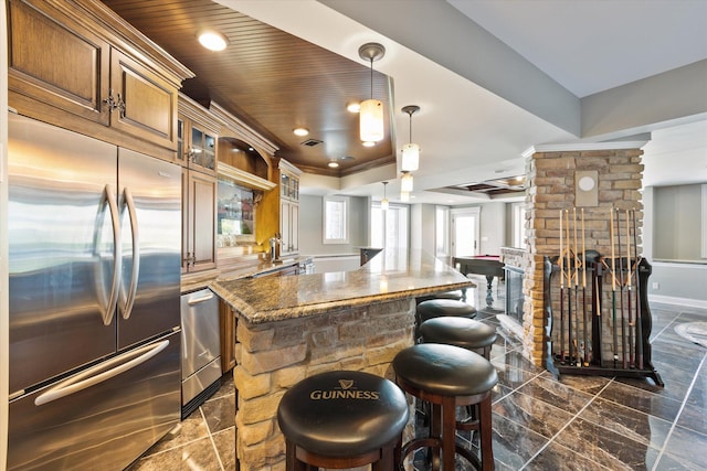 kitchen featuring dark stone countertops, dark tile flooring, built in fridge, kitchen peninsula, and pendant lighting