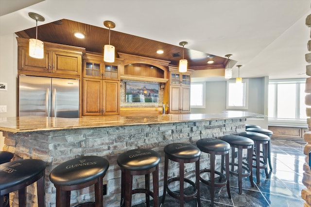 bar featuring hanging light fixtures, light stone counters, and stainless steel refrigerator