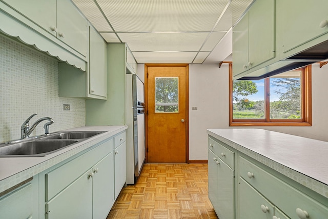 kitchen featuring sink, green cabinetry, a drop ceiling, decorative backsplash, and light parquet flooring