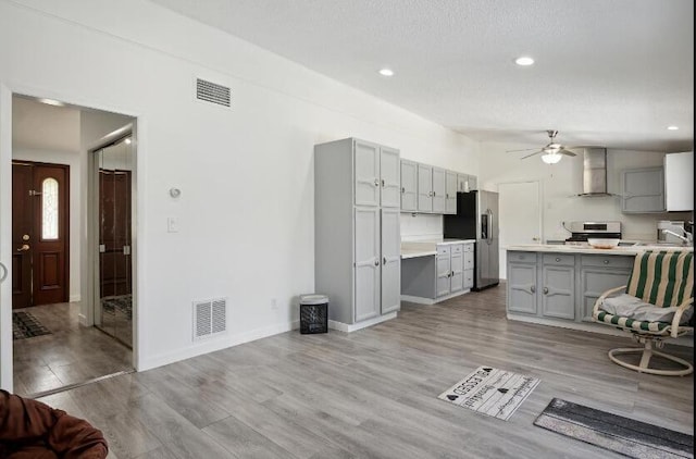 kitchen featuring wall chimney range hood, stainless steel fridge, light wood-type flooring, gray cabinetry, and ceiling fan