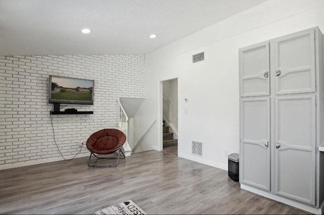 unfurnished room featuring brick wall, hardwood / wood-style floors, a textured ceiling, and lofted ceiling