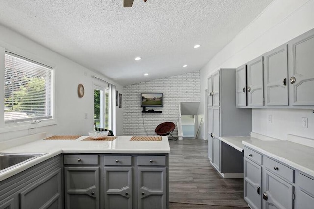 kitchen featuring a textured ceiling, dark wood-type flooring, brick wall, gray cabinets, and vaulted ceiling