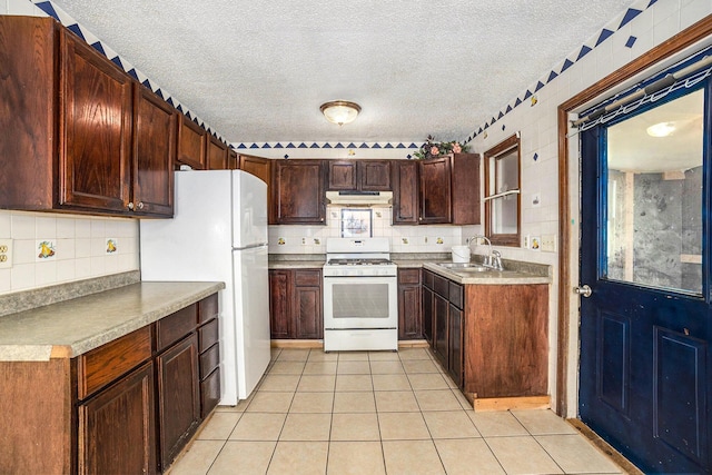 kitchen featuring sink, decorative backsplash, light tile patterned floors, white appliances, and a textured ceiling