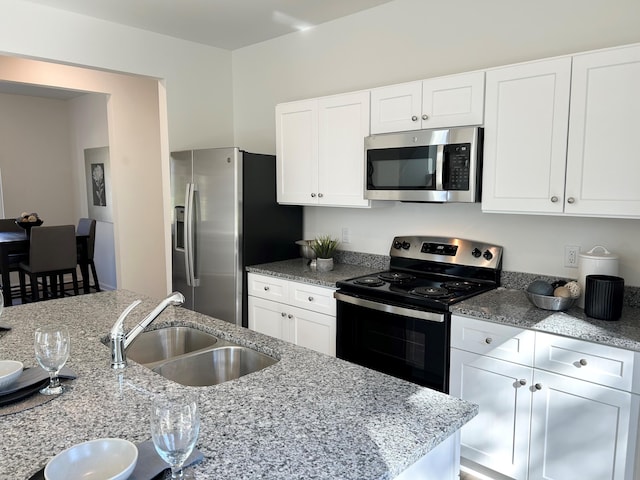 kitchen with white cabinets, light stone countertops, stainless steel appliances, and sink