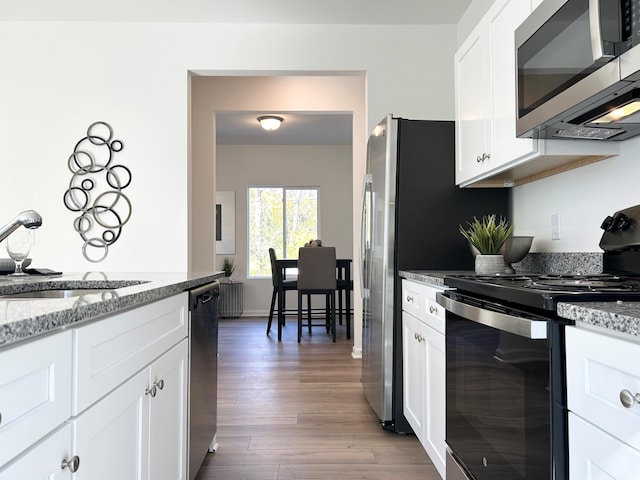 kitchen featuring appliances with stainless steel finishes, white cabinetry, light stone countertops, dark hardwood / wood-style floors, and sink