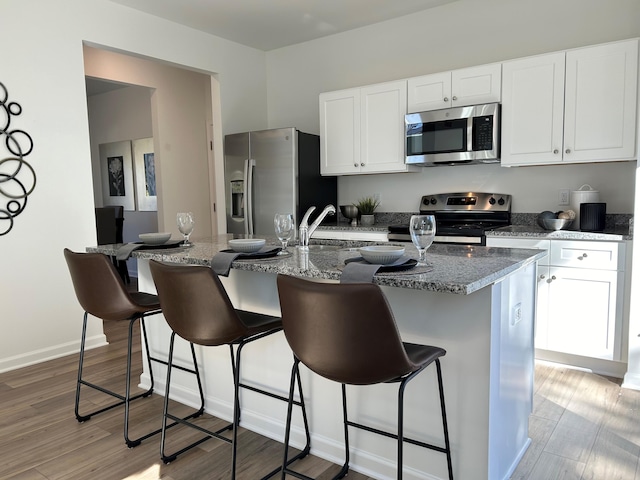 kitchen with white cabinets, light hardwood / wood-style floors, stainless steel appliances, and a kitchen island with sink