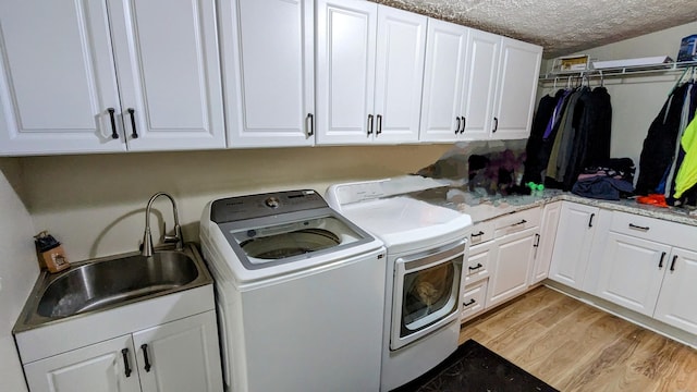 clothes washing area with cabinets, a textured ceiling, sink, light wood-type flooring, and washing machine and dryer