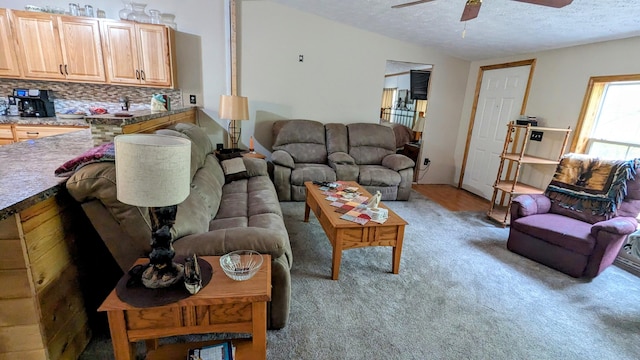 living room with light carpet, ceiling fan, and a textured ceiling