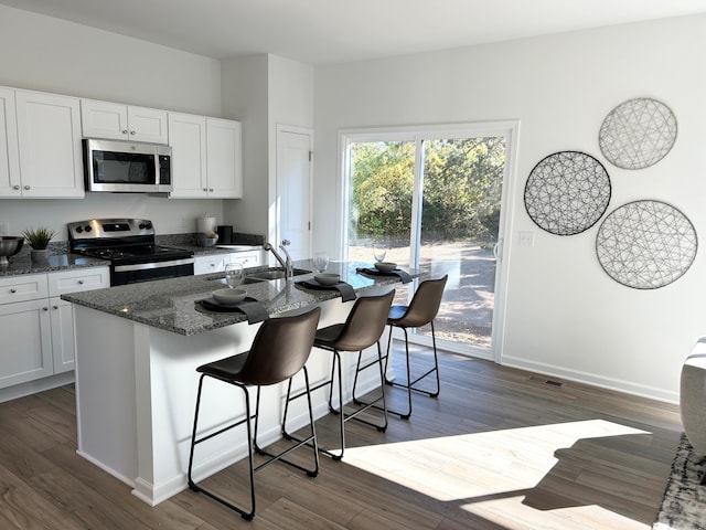 kitchen with a breakfast bar area, dark hardwood / wood-style flooring, white cabinetry, a kitchen island with sink, and stainless steel appliances