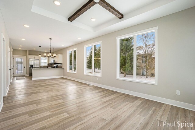 unfurnished living room with beamed ceiling, light hardwood / wood-style flooring, plenty of natural light, and a notable chandelier