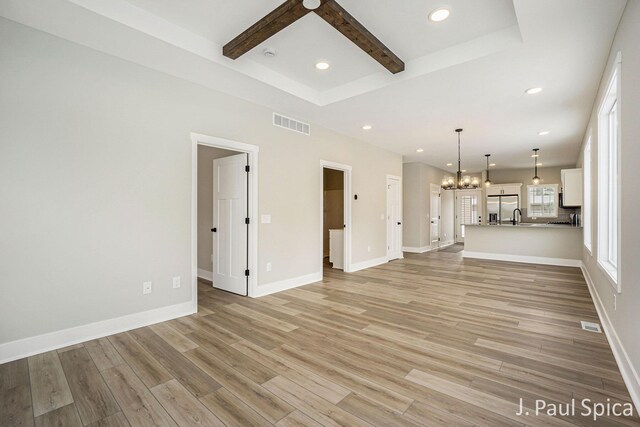 unfurnished living room with beamed ceiling, light wood-type flooring, a chandelier, and sink