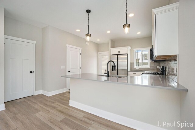 kitchen featuring backsplash, stainless steel fridge, pendant lighting, light hardwood / wood-style floors, and white cabinets