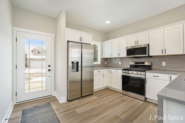 kitchen with backsplash, white cabinetry, stainless steel appliances, and light hardwood / wood-style floors