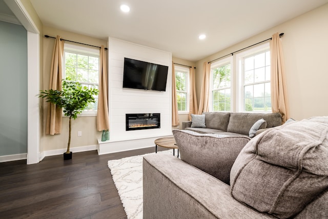 living room with a wealth of natural light, dark wood-type flooring, and a large fireplace