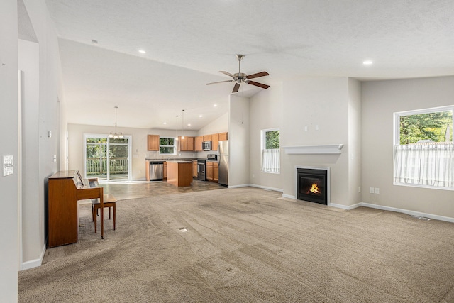 unfurnished living room featuring high vaulted ceiling, ceiling fan with notable chandelier, a wealth of natural light, and light carpet