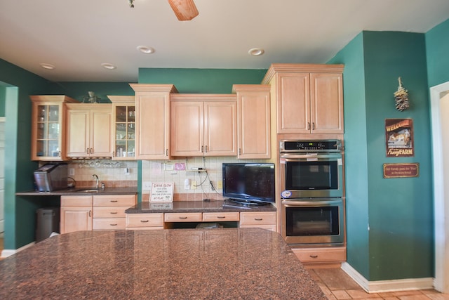 kitchen with dark stone counters, backsplash, ceiling fan, sink, and stainless steel double oven