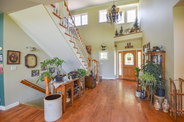 entryway featuring a chandelier, hardwood / wood-style flooring, crown molding, and a towering ceiling