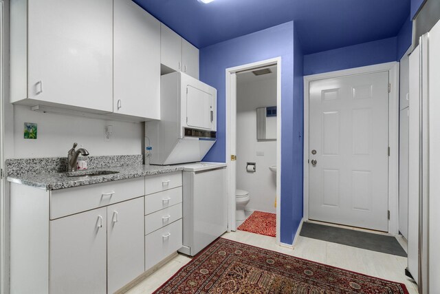 kitchen featuring washer / dryer, white cabinetry, light stone countertops, sink, and light tile floors