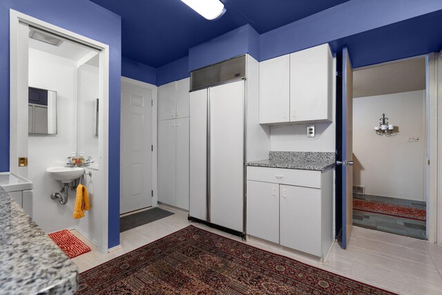 kitchen with white cabinets, paneled built in refrigerator, light tile floors, and light stone countertops