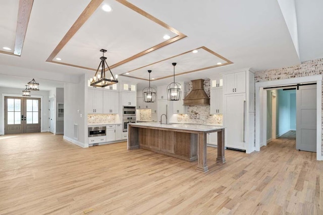 kitchen with a large island, hanging light fixtures, white cabinetry, and custom exhaust hood