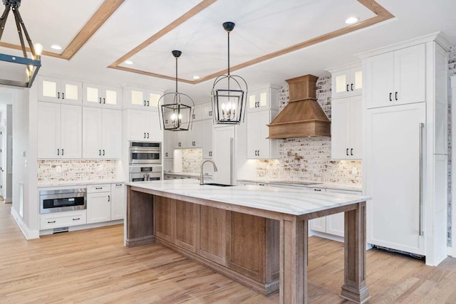 kitchen featuring a large island, light stone counters, custom range hood, white cabinets, and a raised ceiling