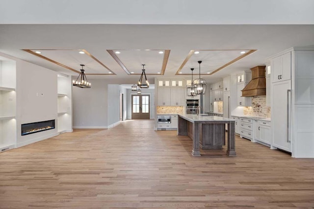 kitchen featuring a spacious island, white cabinetry, custom exhaust hood, and backsplash