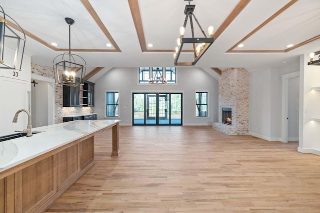 kitchen with a stone fireplace, an inviting chandelier, hanging light fixtures, light stone countertops, and light wood-type flooring