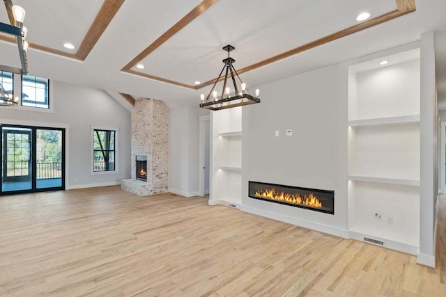 unfurnished living room featuring an inviting chandelier, a fireplace, built in features, and light hardwood / wood-style floors