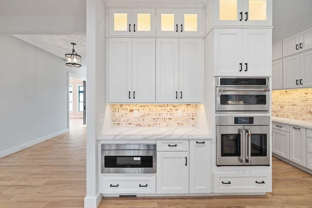 kitchen with pendant lighting, white cabinetry, tasteful backsplash, light hardwood / wood-style floors, and stainless steel double oven