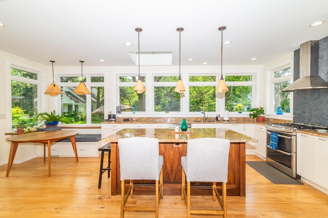 kitchen with decorative light fixtures, wall chimney range hood, double oven range, and plenty of natural light