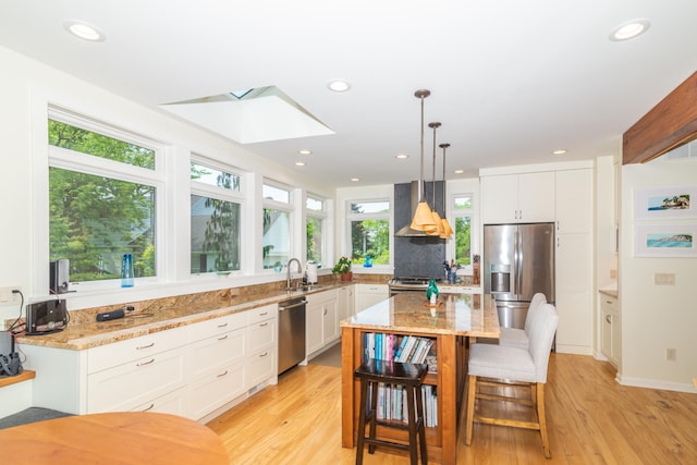 kitchen with light stone counters, a kitchen island, a skylight, wall chimney exhaust hood, and appliances with stainless steel finishes