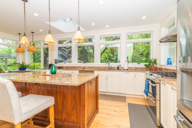 kitchen featuring stainless steel appliances, light wood-type flooring, light stone counters, white cabinets, and a skylight