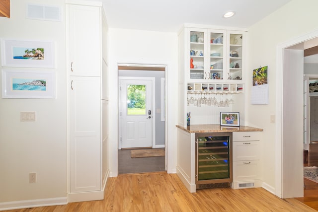 bar featuring light stone counters, wine cooler, white cabinets, and light wood-type flooring