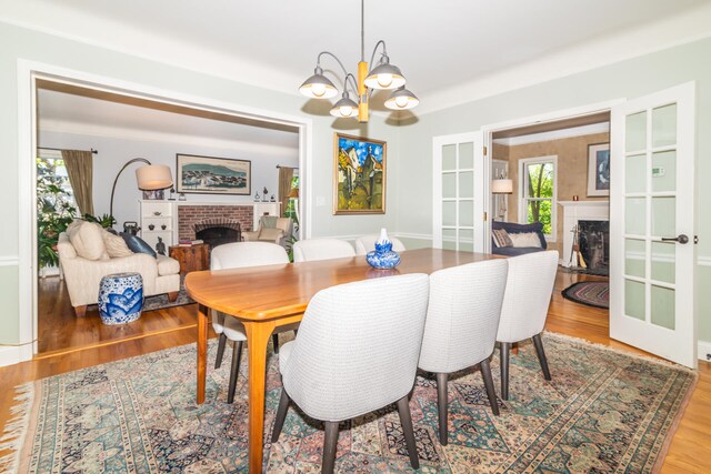 dining area featuring french doors, wood-type flooring, an inviting chandelier, and a fireplace