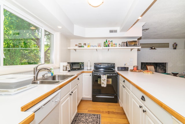 kitchen with light hardwood / wood-style flooring, black appliances, white cabinets, a brick fireplace, and sink