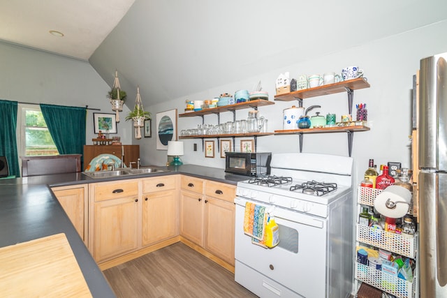 kitchen featuring gas range gas stove, vaulted ceiling, light hardwood / wood-style flooring, stainless steel fridge, and sink