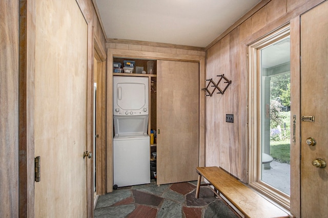 clothes washing area featuring stacked washer / dryer and wooden walls