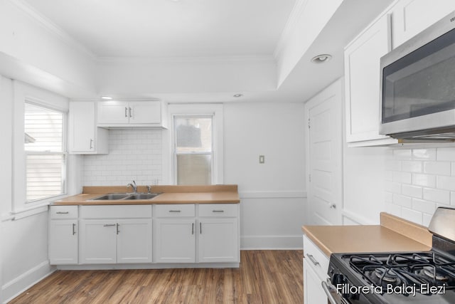 kitchen featuring white cabinetry, ornamental molding, appliances with stainless steel finishes, hardwood / wood-style floors, and sink