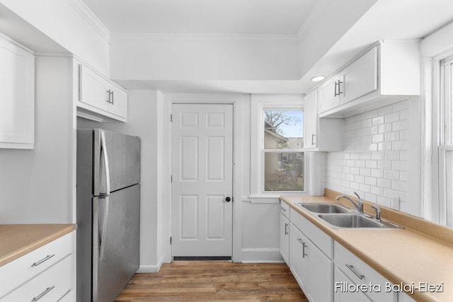 kitchen with white cabinetry, hardwood / wood-style floors, stainless steel refrigerator, sink, and tasteful backsplash