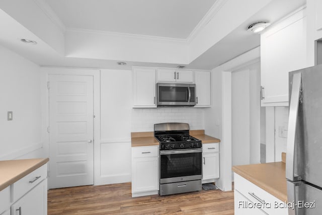 kitchen featuring white cabinetry, ornamental molding, stainless steel appliances, hardwood / wood-style floors, and tasteful backsplash