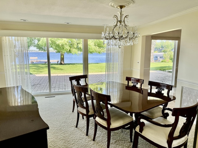 dining area featuring carpet flooring, a water view, a notable chandelier, ornamental molding, and a healthy amount of sunlight