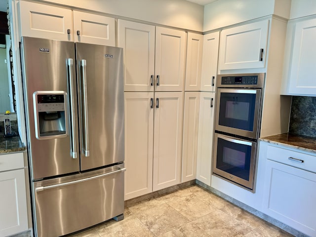 kitchen featuring white cabinetry, appliances with stainless steel finishes, backsplash, and dark stone counters