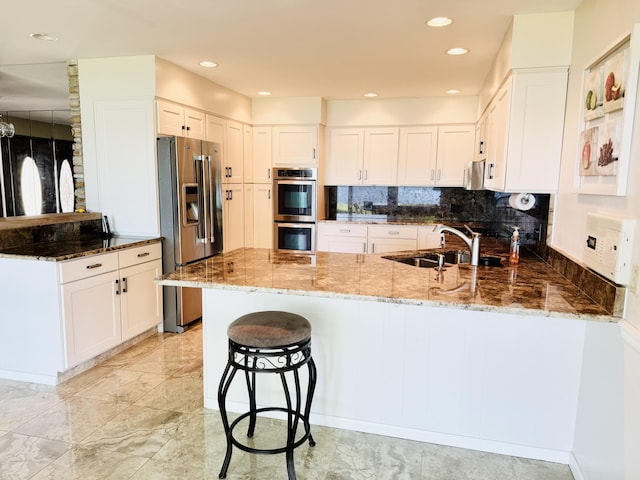 kitchen featuring stainless steel appliances, kitchen peninsula, sink, and stone countertops