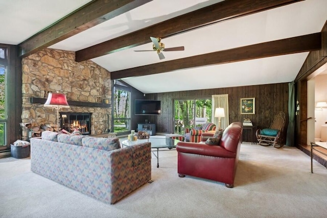 carpeted living room featuring vaulted ceiling with beams, ceiling fan, a stone fireplace, and wood walls