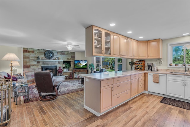 kitchen with sink, light hardwood / wood-style flooring, white dishwasher, kitchen peninsula, and a fireplace