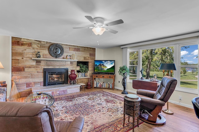 living room featuring hardwood / wood-style floors, a stone fireplace, and ceiling fan