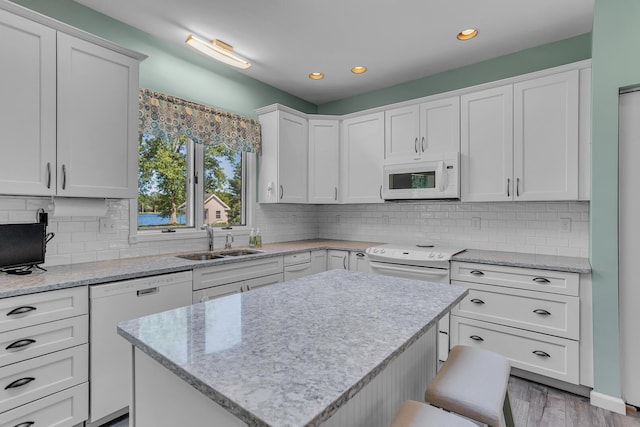 kitchen with sink, white appliances, white cabinetry, hardwood / wood-style floors, and a kitchen island