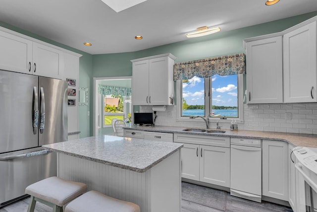 kitchen featuring stainless steel refrigerator, white cabinetry, sink, decorative backsplash, and range